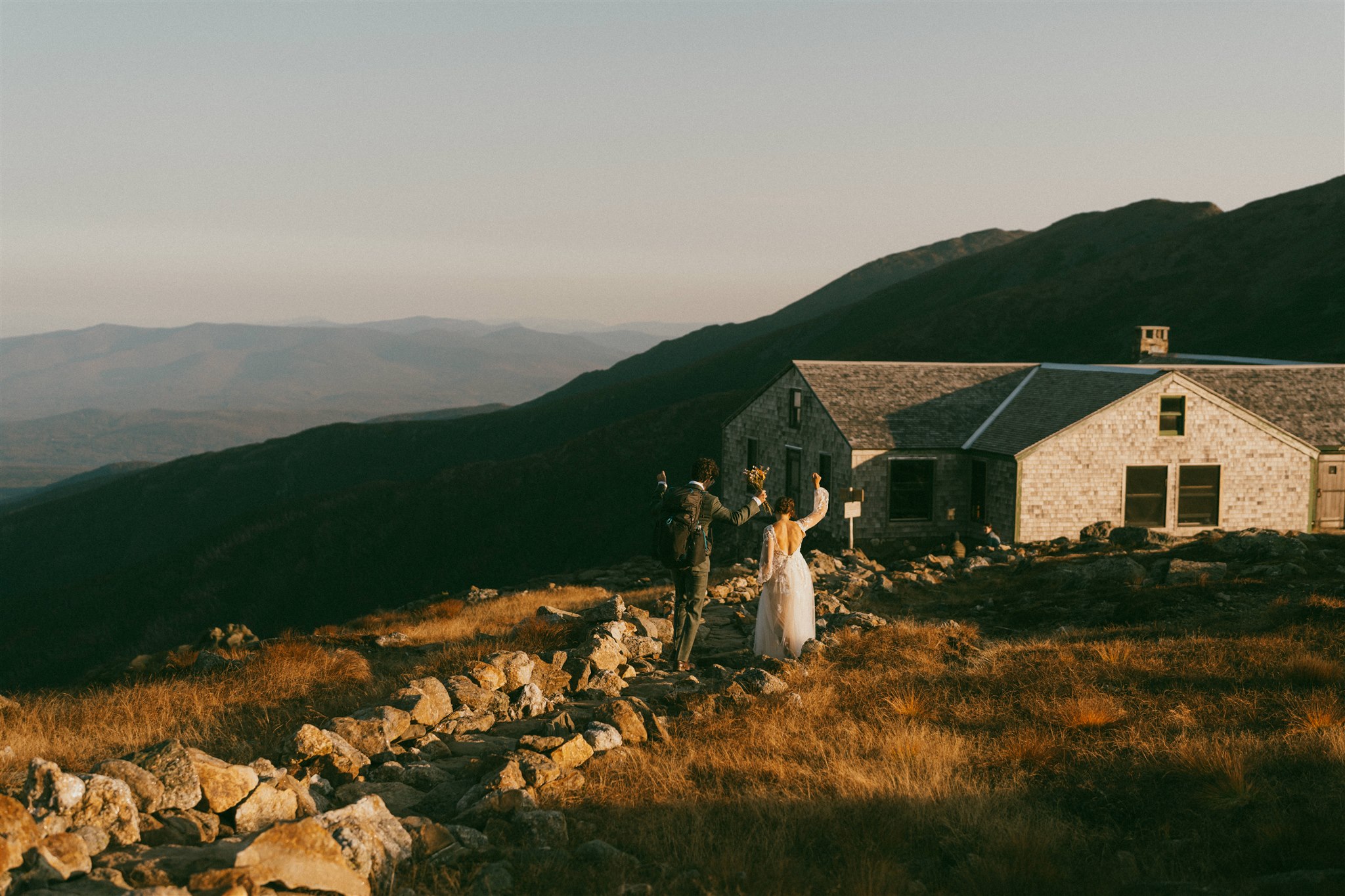 A couple in wedding attire celebrates at sunrise as they walk towards the Lakes of the Clouds hut in the White Mountains of New Hampshire after eloping. 