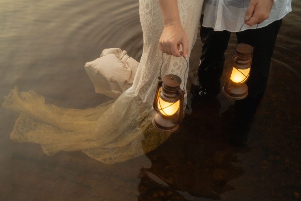 Couple holding lanterns while standing together in shallow water at dusk