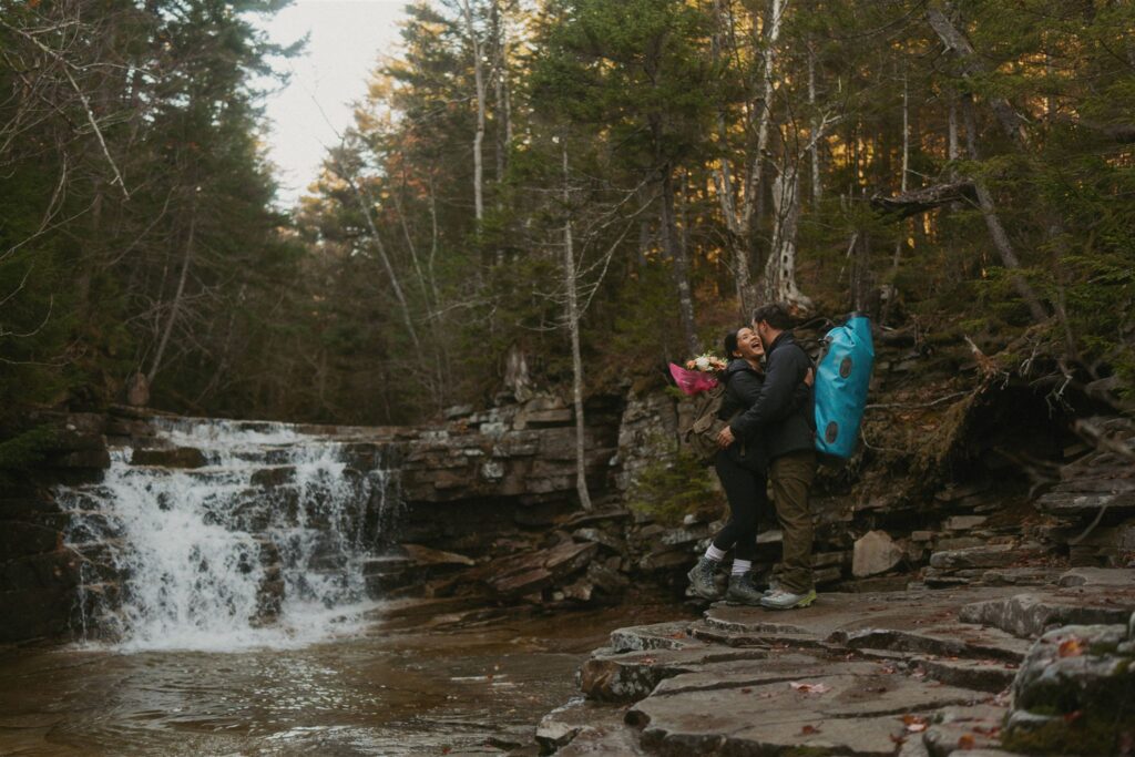 Couple laughing at waterfall while hiking to Arethusa Falls during a White Mountains fall elopement