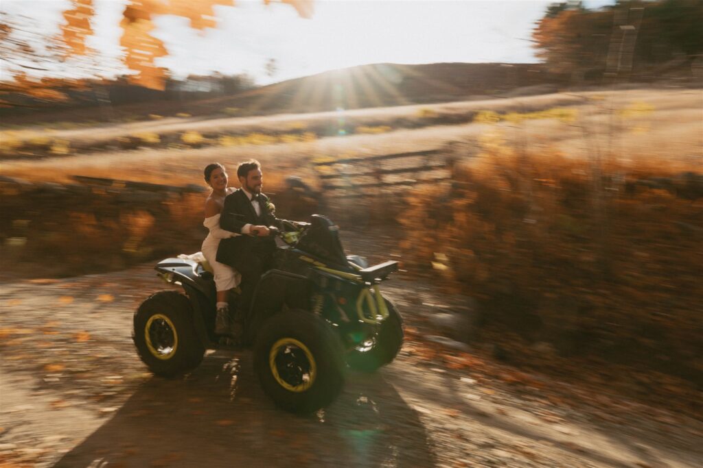 Couple riding an ATV along a dirt road during a fall elopement in the White Mountains of New Hampshire at sunset