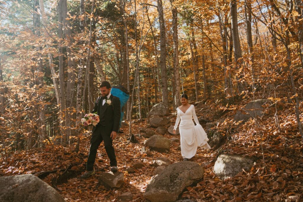 New Hampshire elopement couple hiking out in wedding attire through fall forest after Arethusa Falls ceremony in the White Mountains
