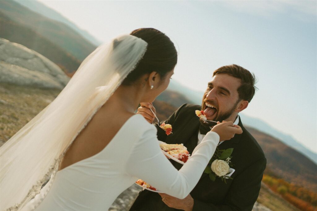 Couple feeding each other cake during sunset elopement on a mountain summit