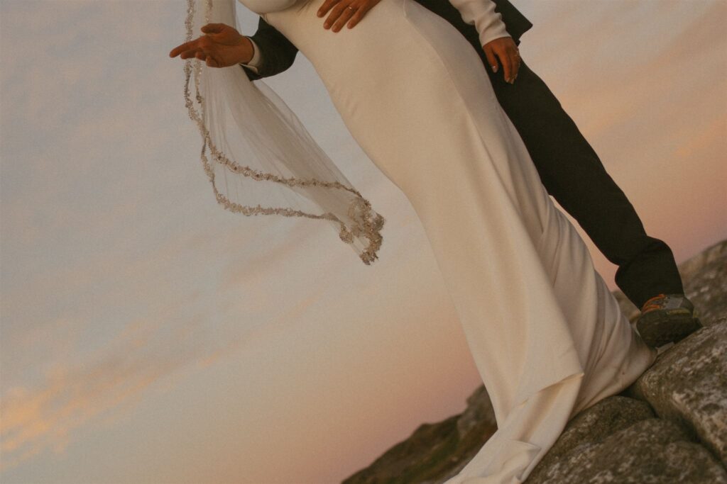 Bride’s dress and veil blowing in the wind on a rocky mountain summit during a sunset elopement in New Hampshire