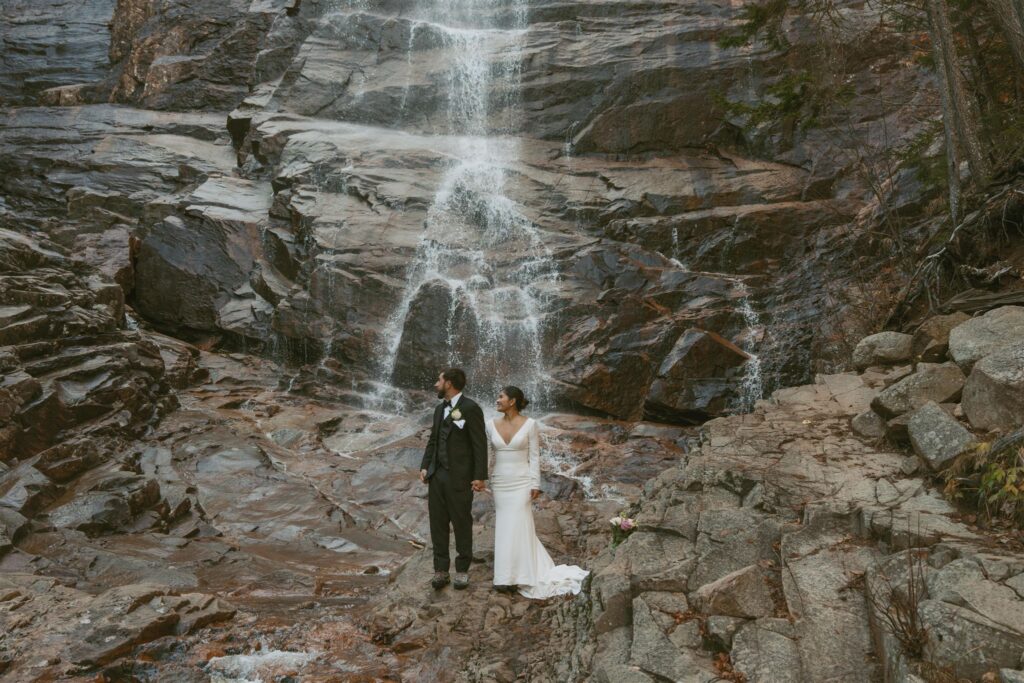 Couple standing at a waterfall during a fall elopement in the White Mountains of New Hampshire