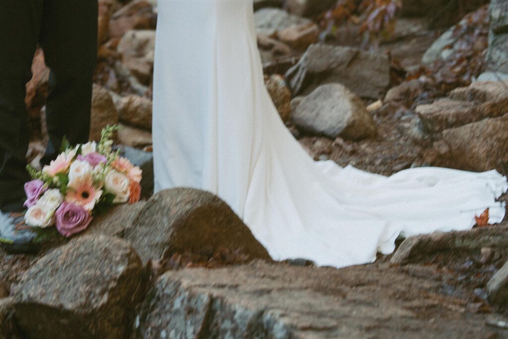 Wedding dress and bouquet resting on rocks at the base of a waterfall in late fall