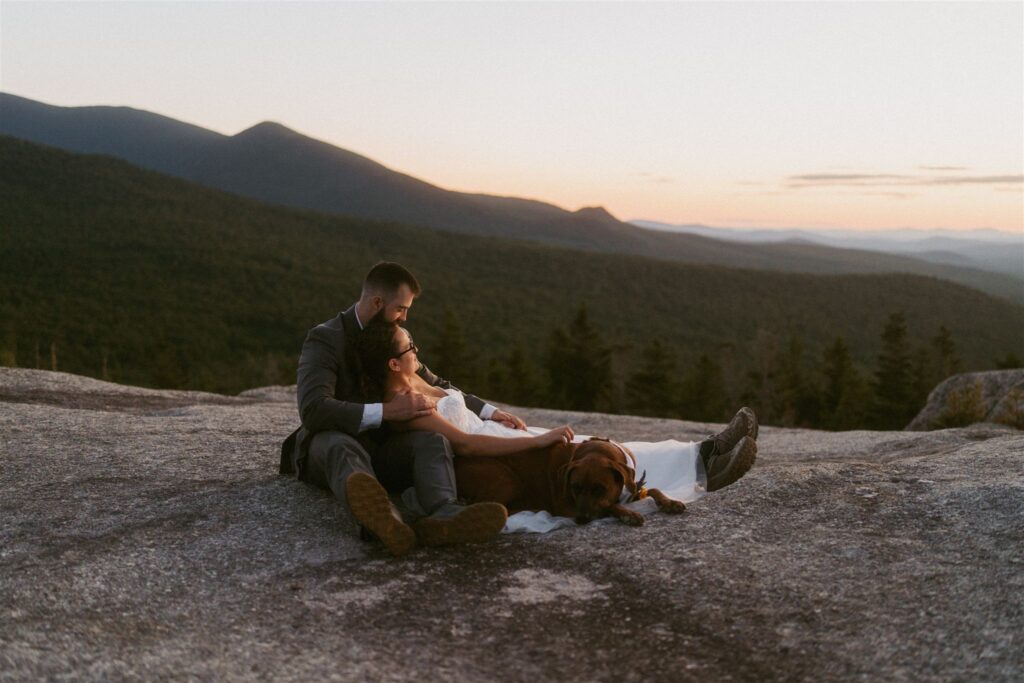 Couple relaxing with their dog on a mountain overlook after their elopement ceremony in New Hampshire